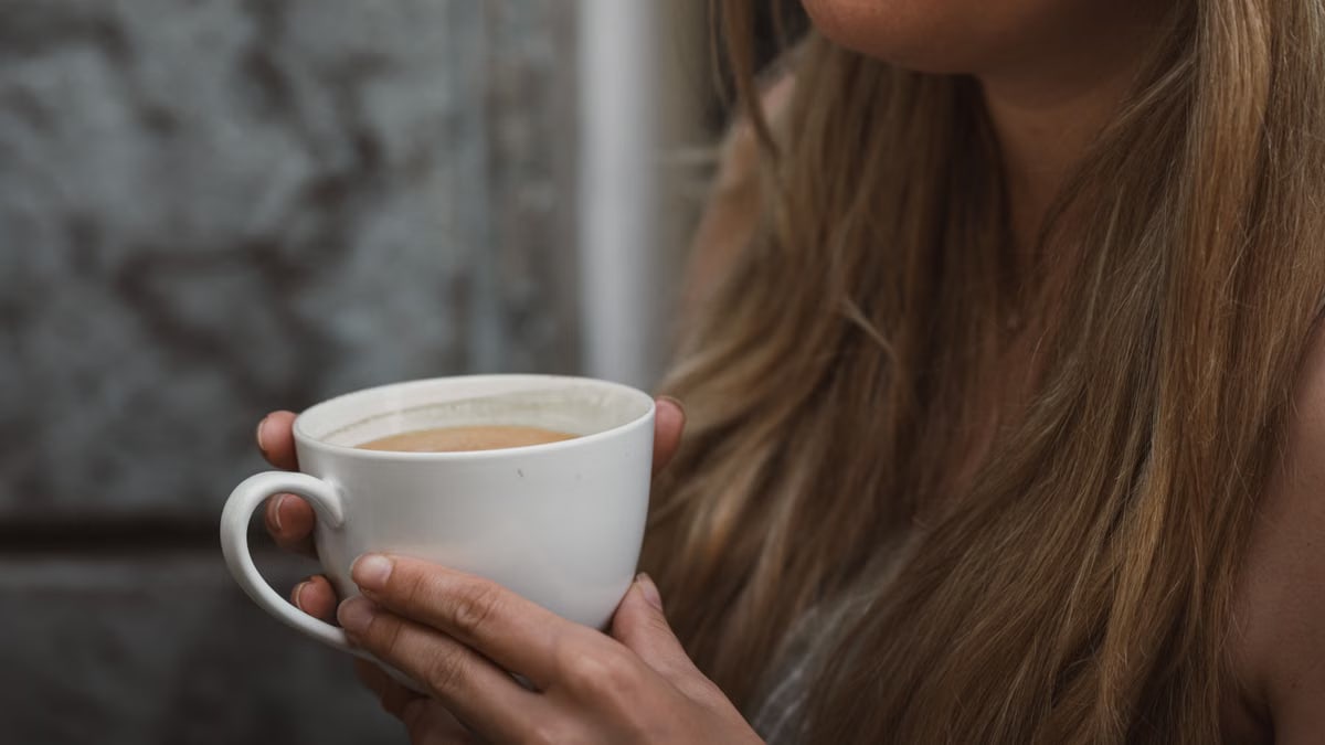 A woman with long blonde hair holding a coffee cup, enjoying a quiet morning outdoors in Graz, Austria.